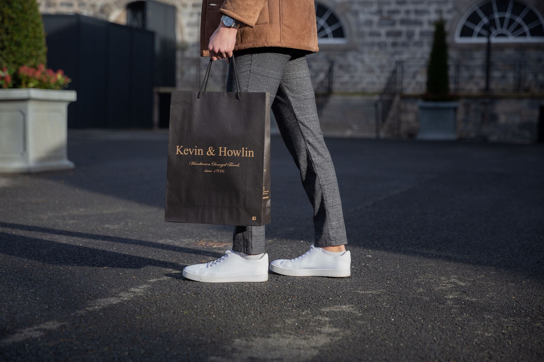 Black matt laminated portrait paper bag with gold foil logo, black rope handles, and reinforced top edge.