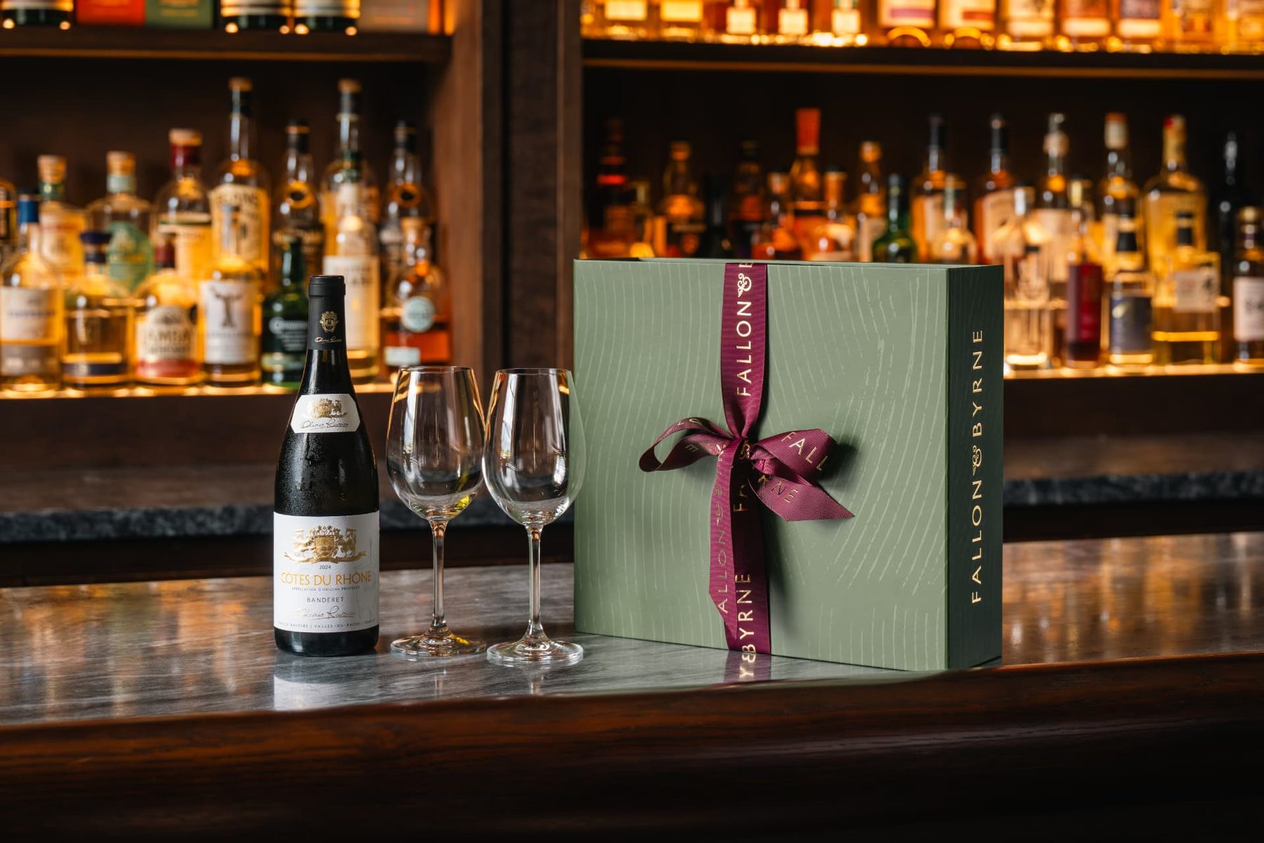 Sage green rigid gift box, woodgrain texture, burgundy branded ribbon tied in a bow. Features the 'FALLON & BYRNE' logo on the front and side.
