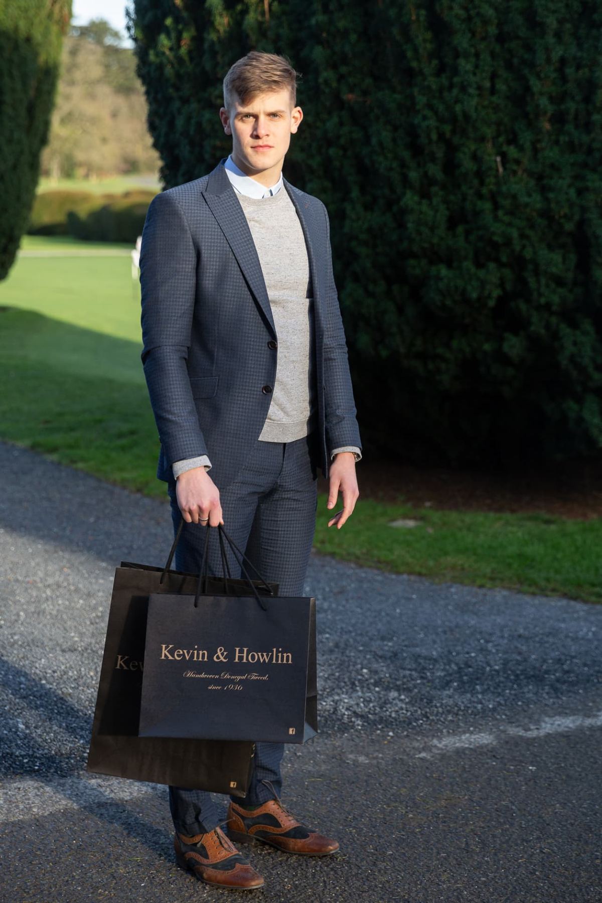 Two black matt laminated paper bags with gold foil text logo and black rope handles, one slightly larger than the other, in portrait format.