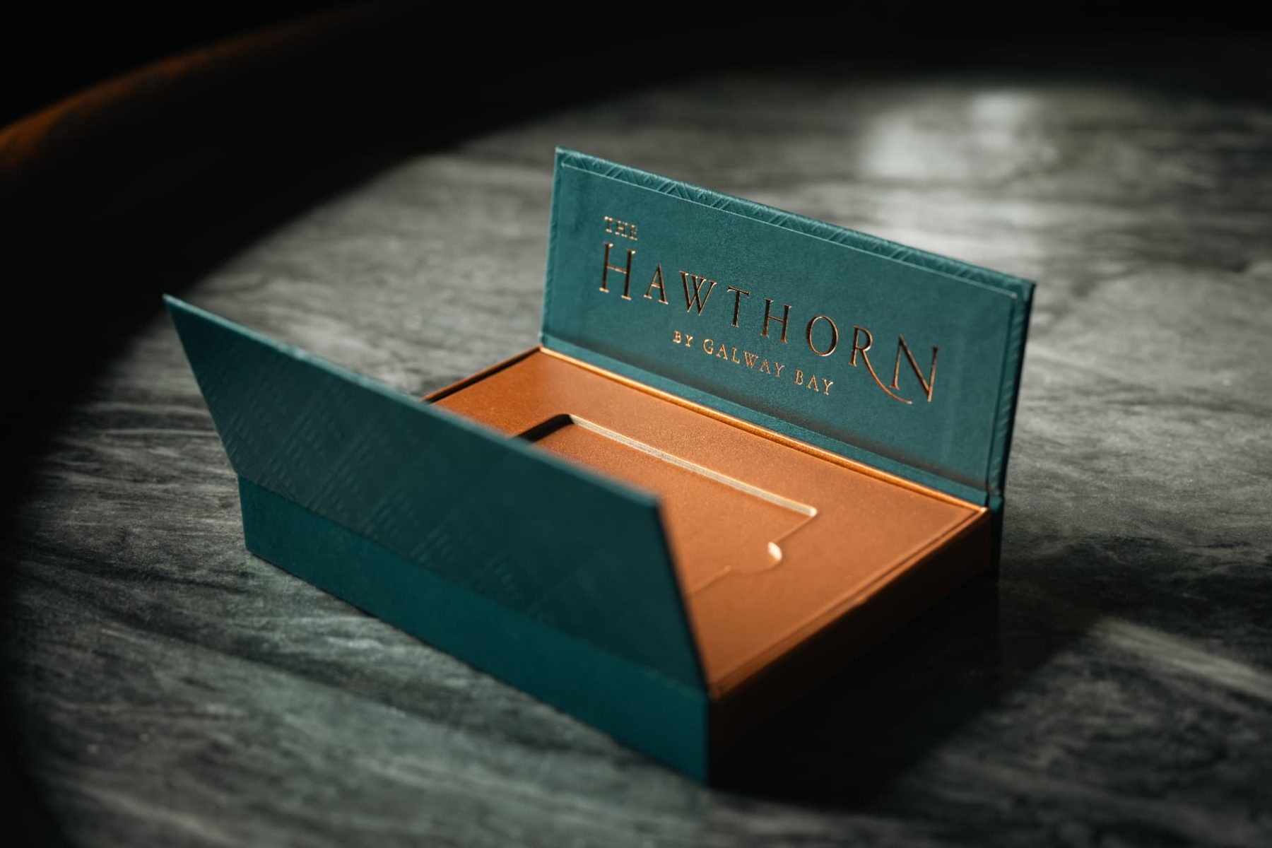 Teal rigid gift box with textured finish, copper foil interior, copper foil stamped logo on lid, magnetic flap closure, open revealing gift card insert.