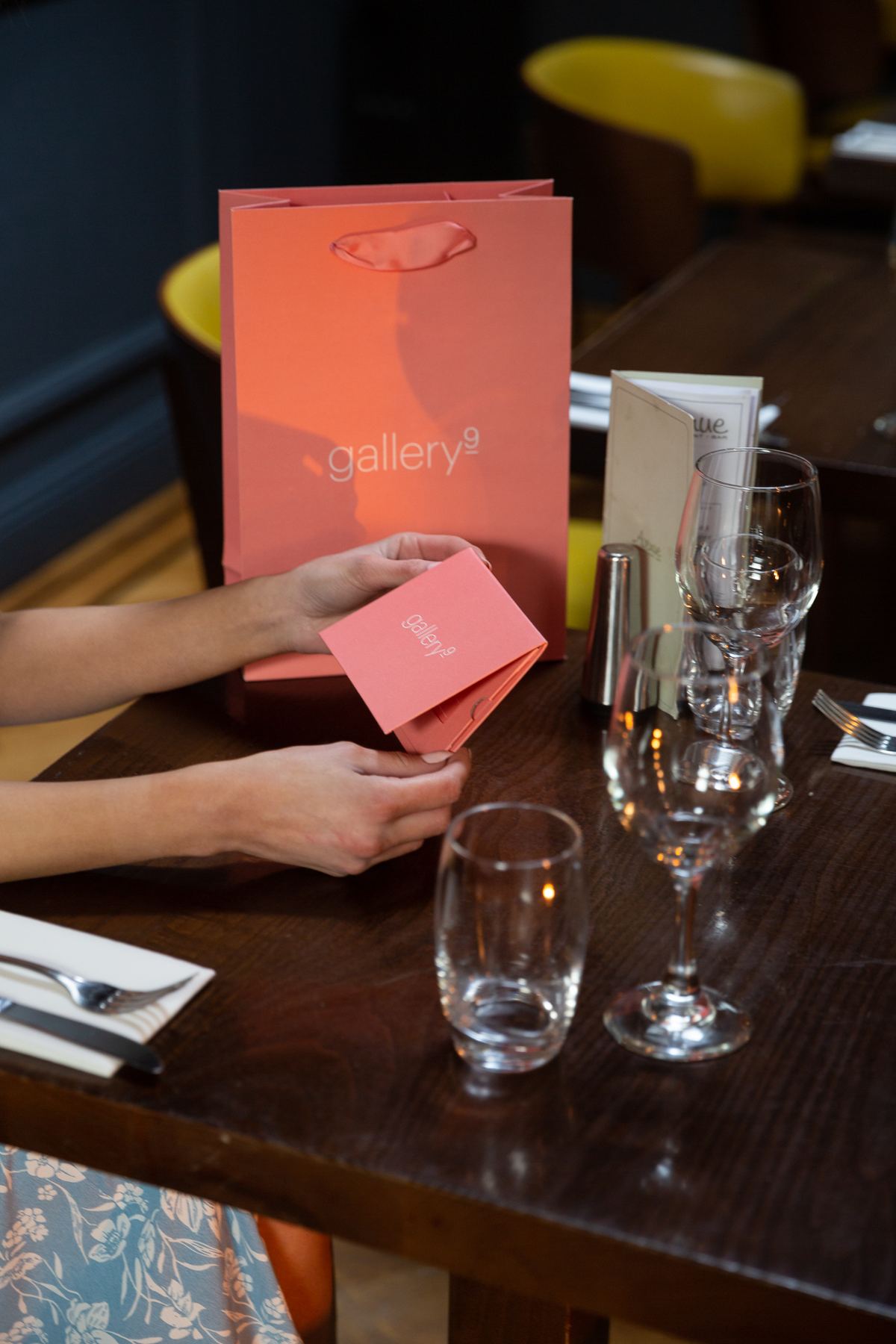 A coral pink matt laminated portrait paper bag with die cut ribbon handles and a small matching folded card, both featuring a white 'gallery9' logo.