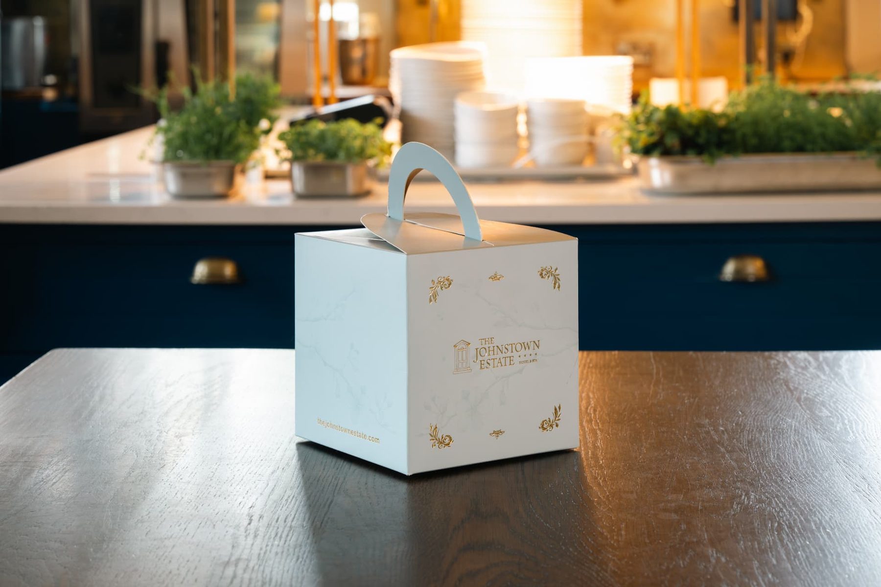 White marble effect gift box with an integrated arched top handle, featuring gold foil logo and decorative accents for The Johnstown Estate.