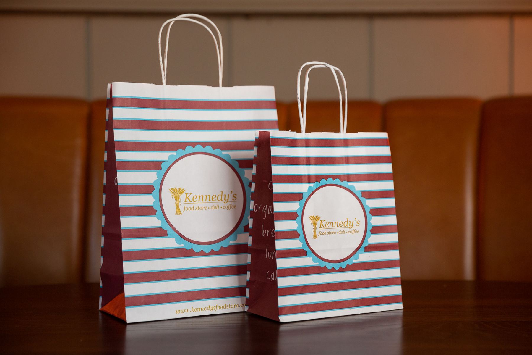 Two white paper bags with red and thin blue horizontal stripes, a circular Kennedy's Food Store logo, and twisted white paper handles.