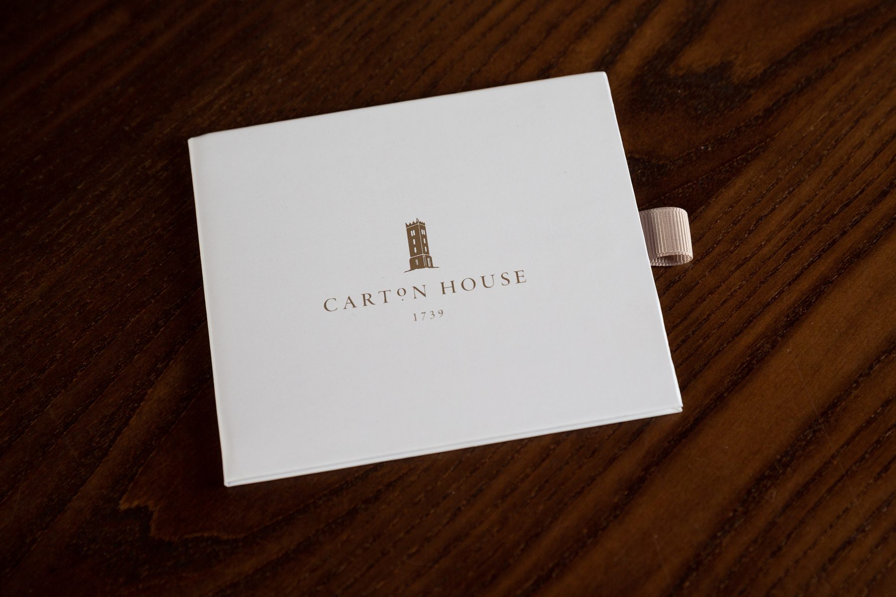Small white matt laminated rigid box with a gold foil logo, "Carton House 1739", and a light pink ribbon pull closure.