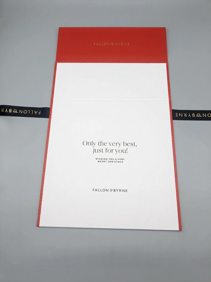 Opened red and white Fallon and Byrne rigid gift box laid flat with printed interior message and black ribbon.