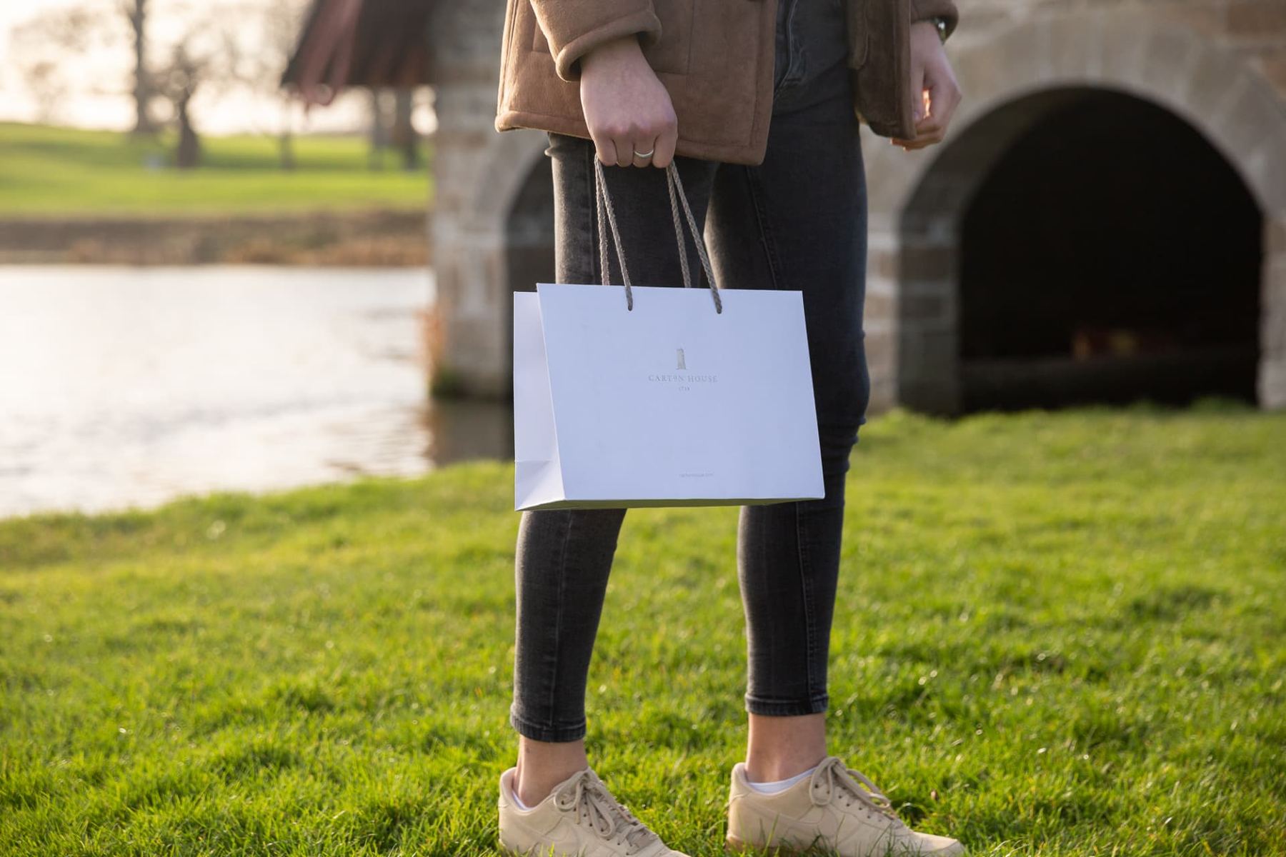 White matt laminated portrait paper bag with grey twisted rope handles and a discreet 'CARTON HOUSE' logo printed in dark grey.