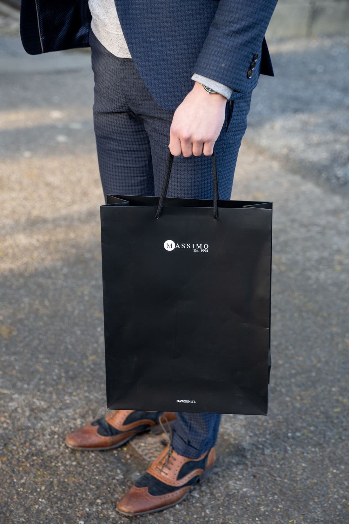 Black matt laminated portrait rope handle paper bag with white printed Massimo logo and 'Dawson St.' detail. Black woven rope handles.
