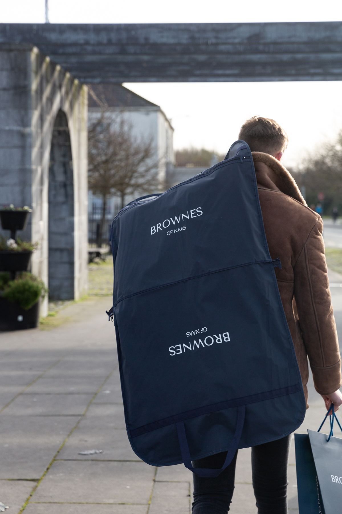 Navy garment cover bag with white 'Brownes of Naas' logo printing, featuring a top loop for hanging and base carry handles.