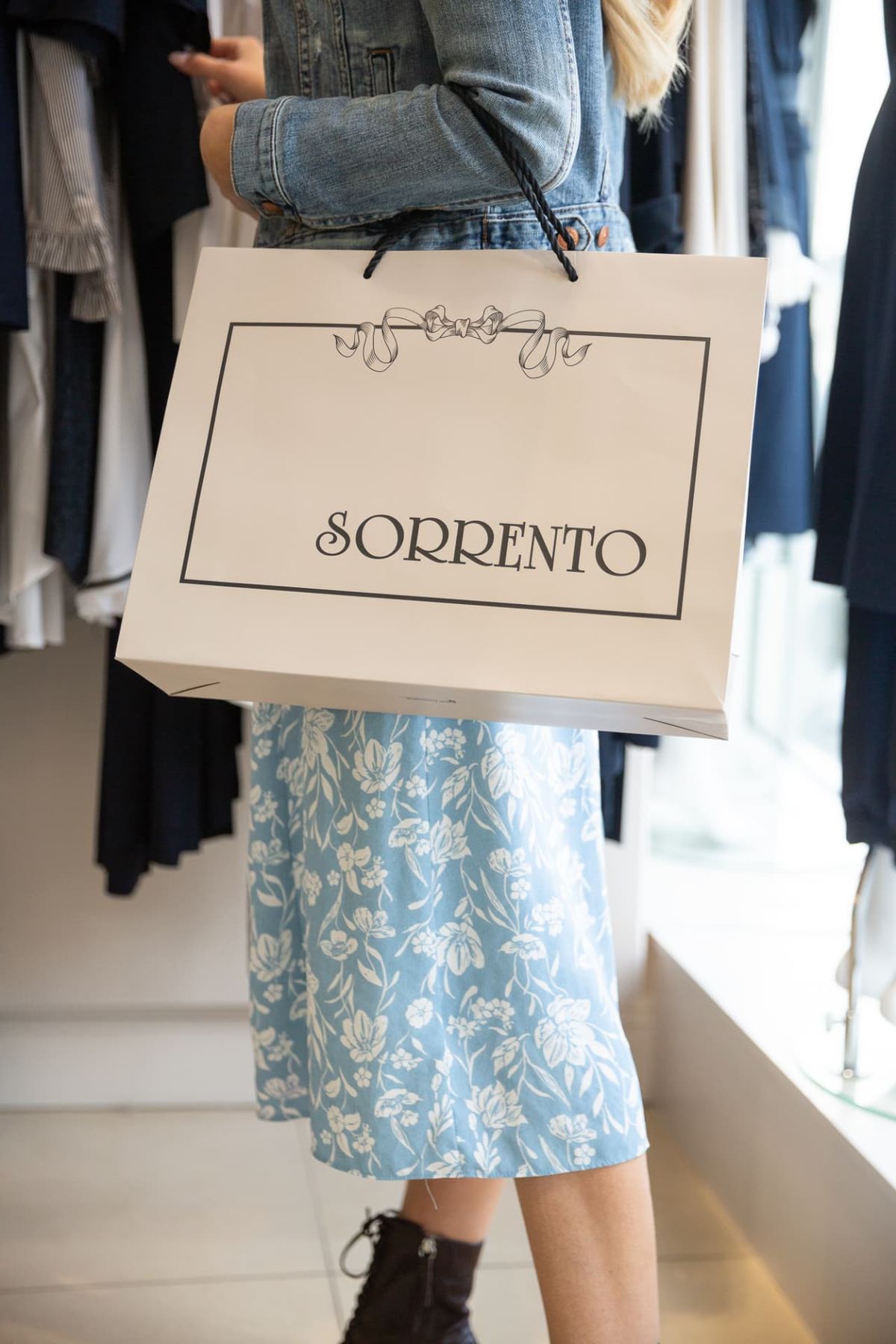 Cream landscape paper carrier bag with black screen printed logo, decorative black border, and black twisted rope handles.