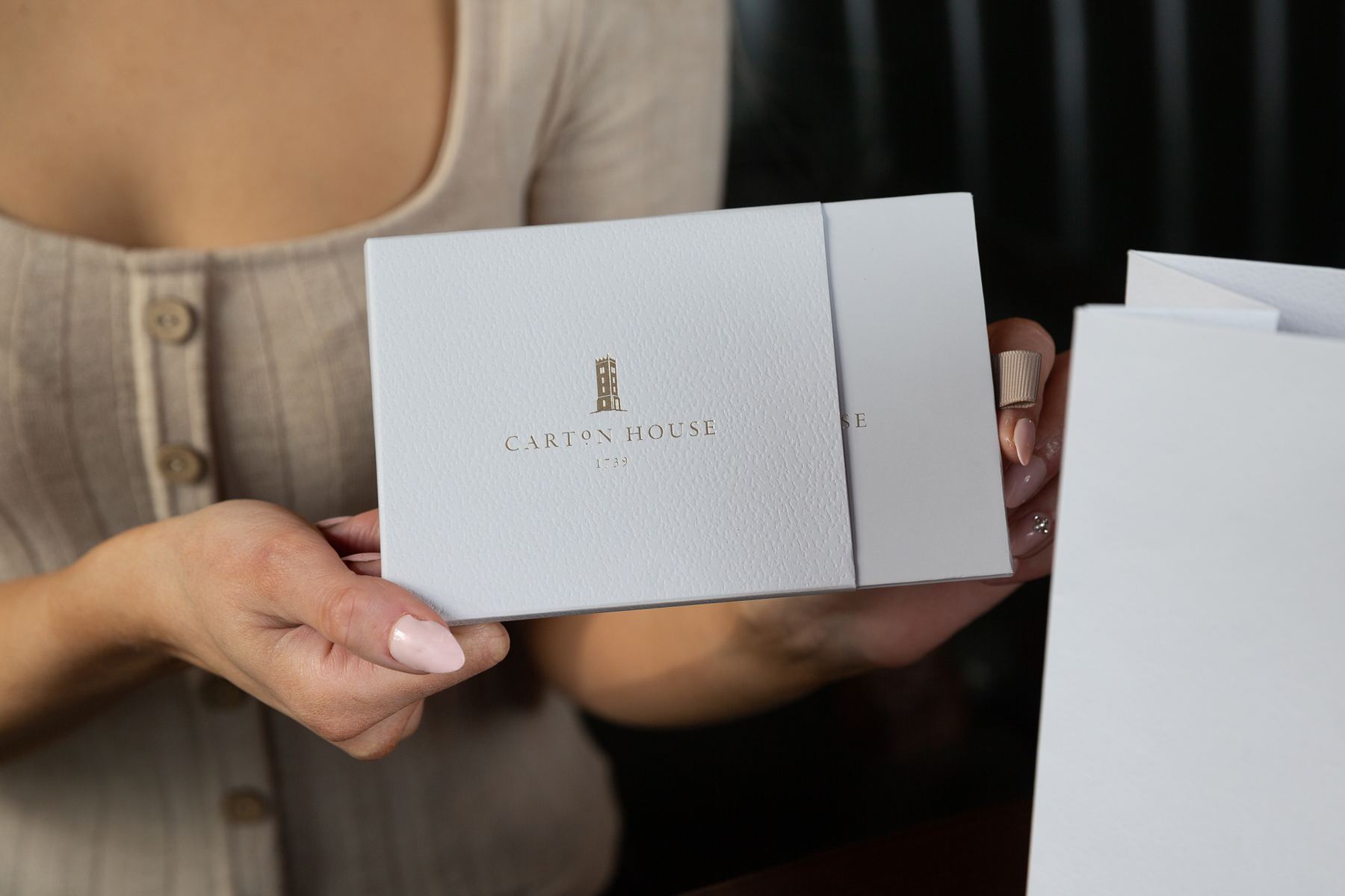 Textured white rigid gift card box with a matching sleeve, featuring a gold foil stamped logo and text on the front.