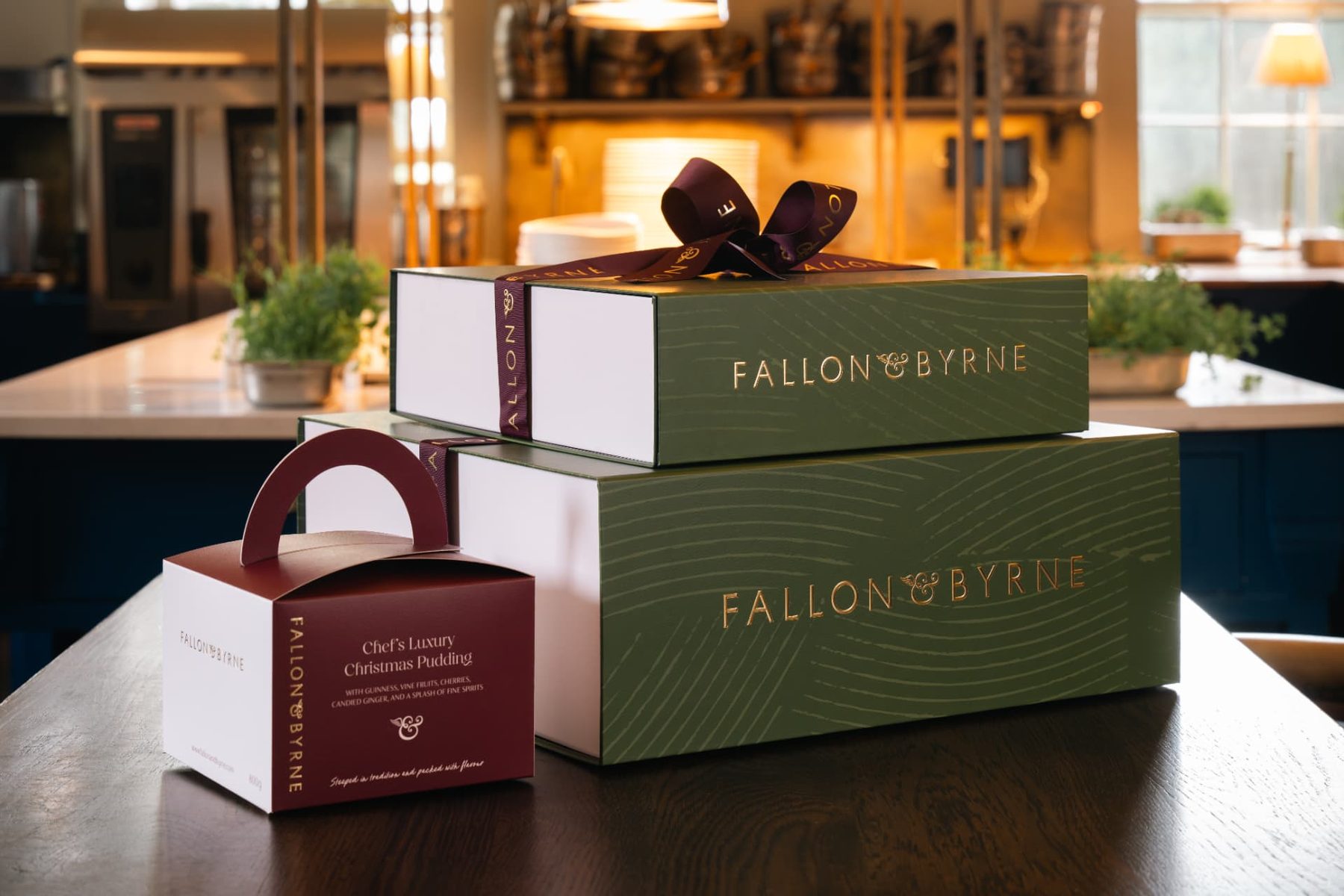 Two green and white rigid gift boxes with gold foil logo and subtle wave pattern, and a smaller red and white carton with a handle.