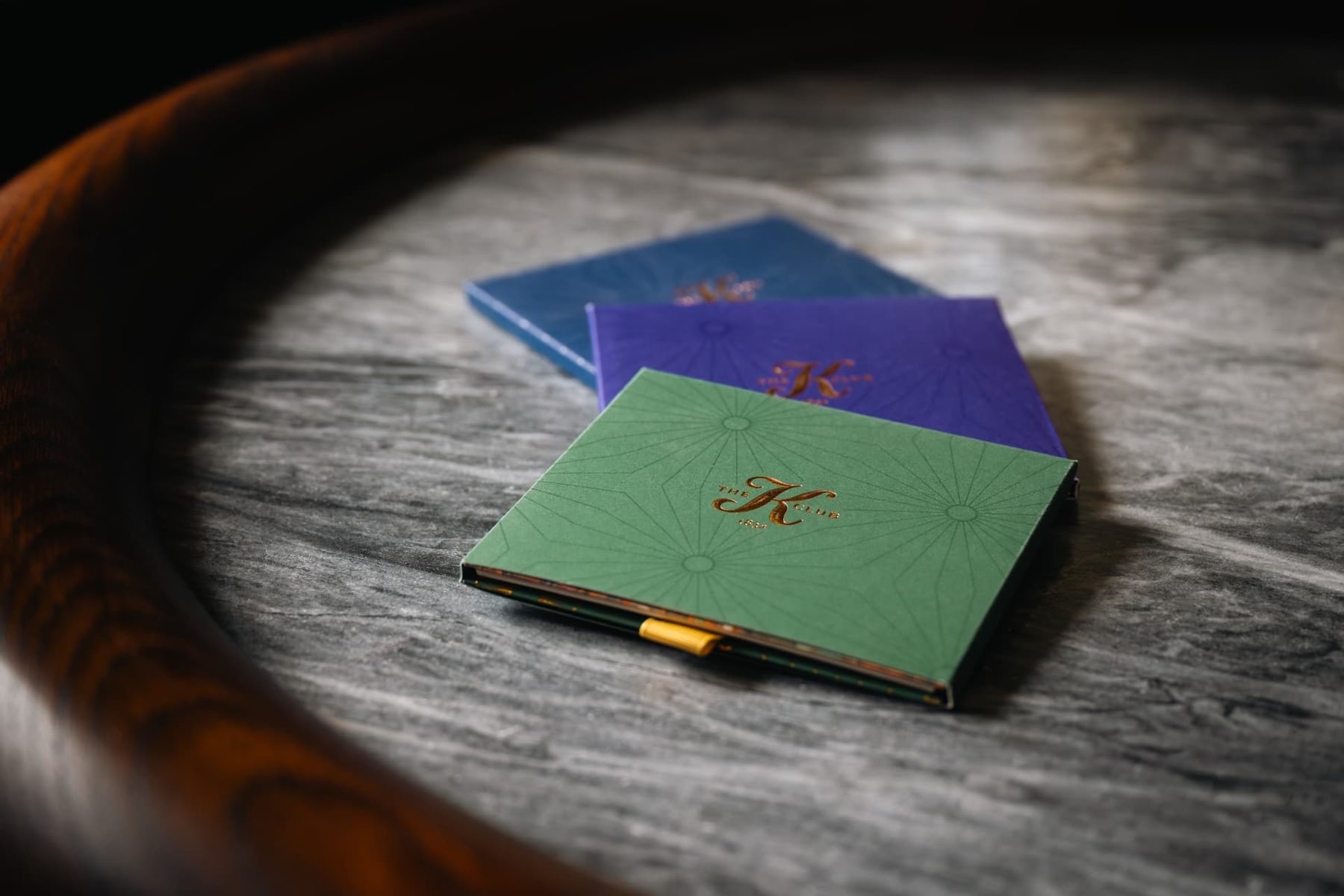 Three small rigid gift card boxes in green, purple, and blue, with gold foil printed monograms and a subtle geometric pattern.