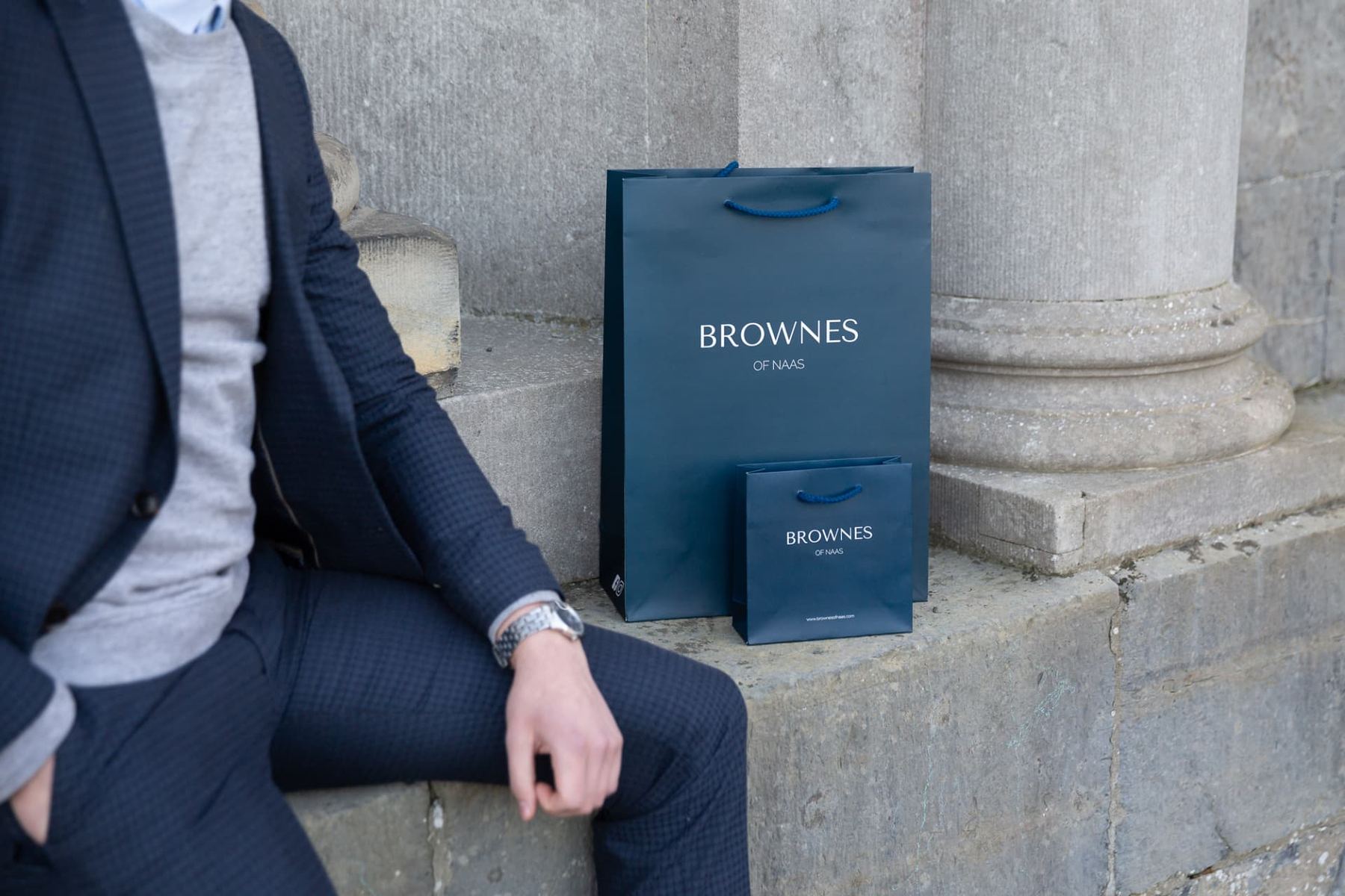 Two navy matt laminated paper bags with white foil stamped Browne's of Naas logo and navy rope handles in varying sizes.