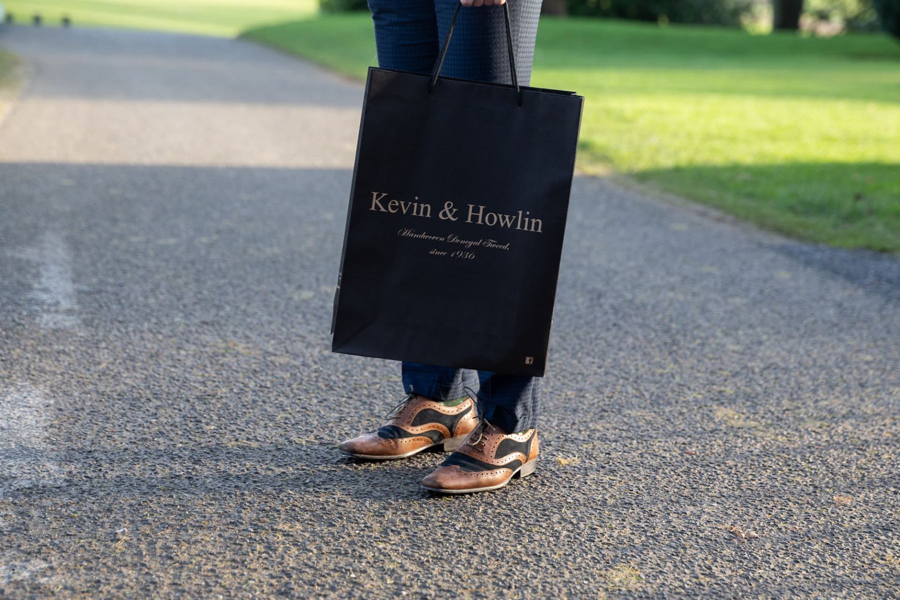 Black matt laminated paper carrier bag with a metallic gold printed logo and black cord rope handles.