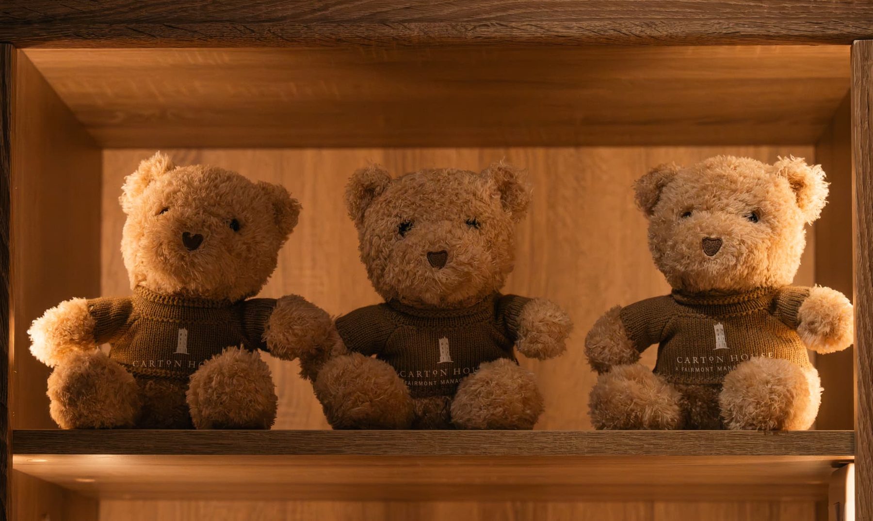 Three branded teddy bears wearing knitted jumpers with an embroidered hotel tower logo, displayed on a boutique retail shelf.