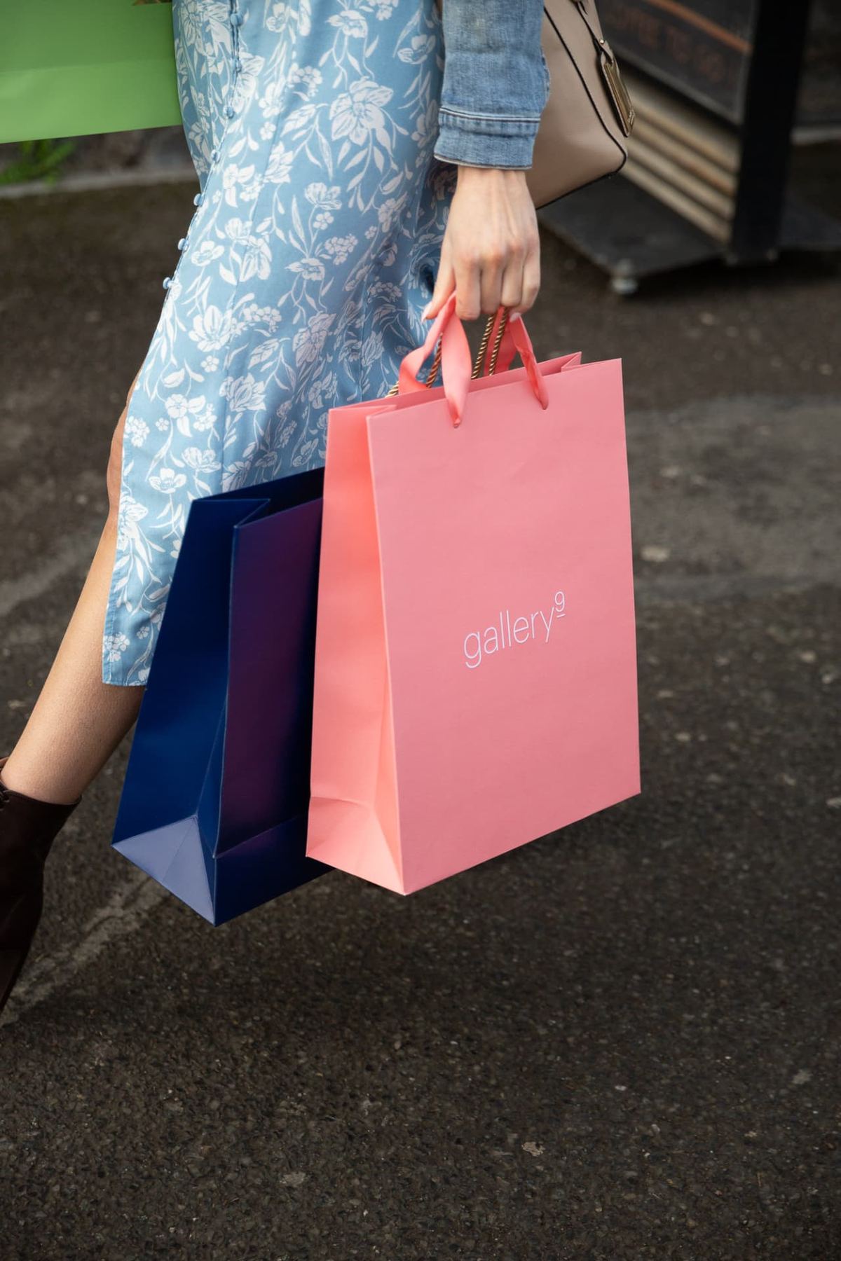 Two matt laminated paper bags, one coral pink with white logo print, the other navy blue. Both have matching ribbon handles.