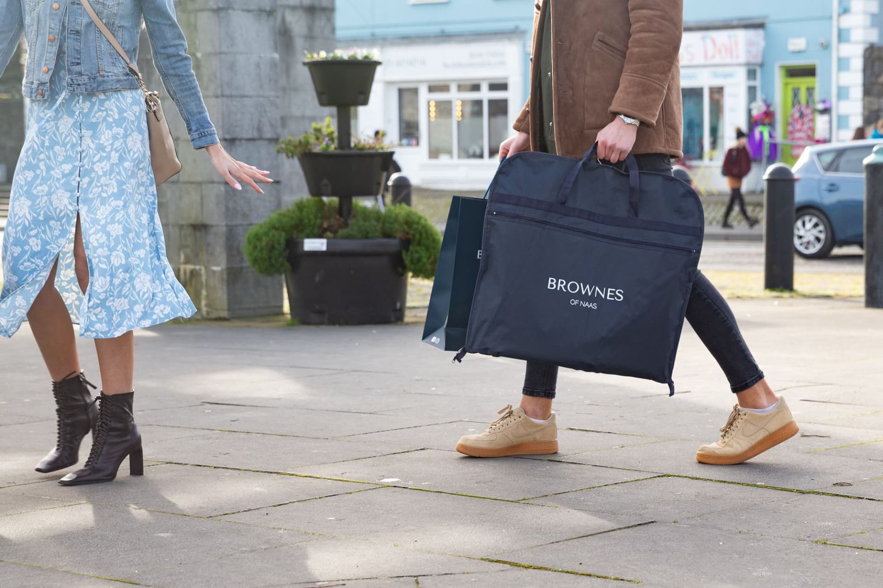 Navy garment carrier bag with black webbing handles and a prominent white printed logo on the front. Features a zip closure.