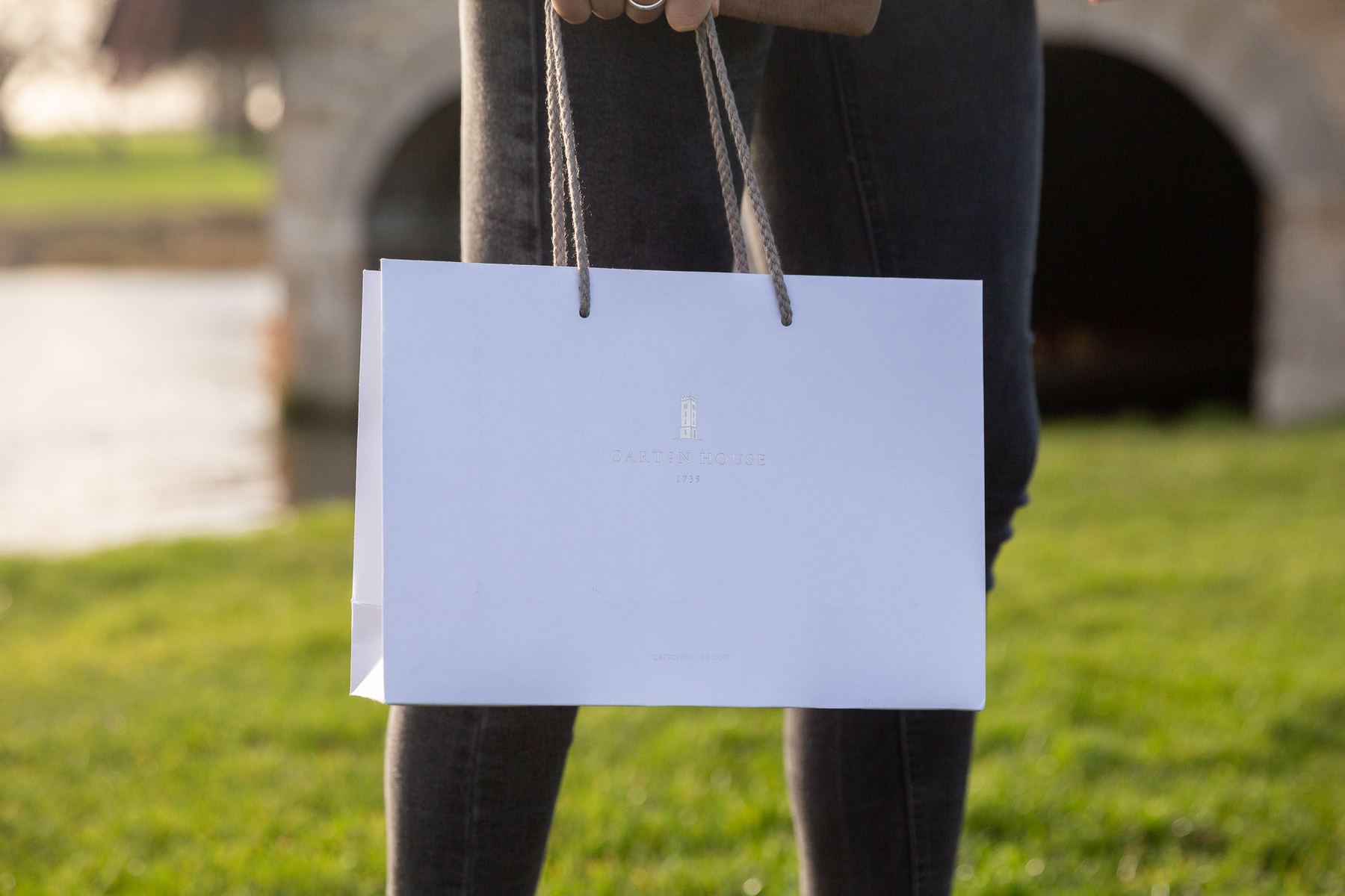 White matt laminated landscape paper bag with gold foil 'Carton House' logo and complementary twisted rope handles, knotted inside.