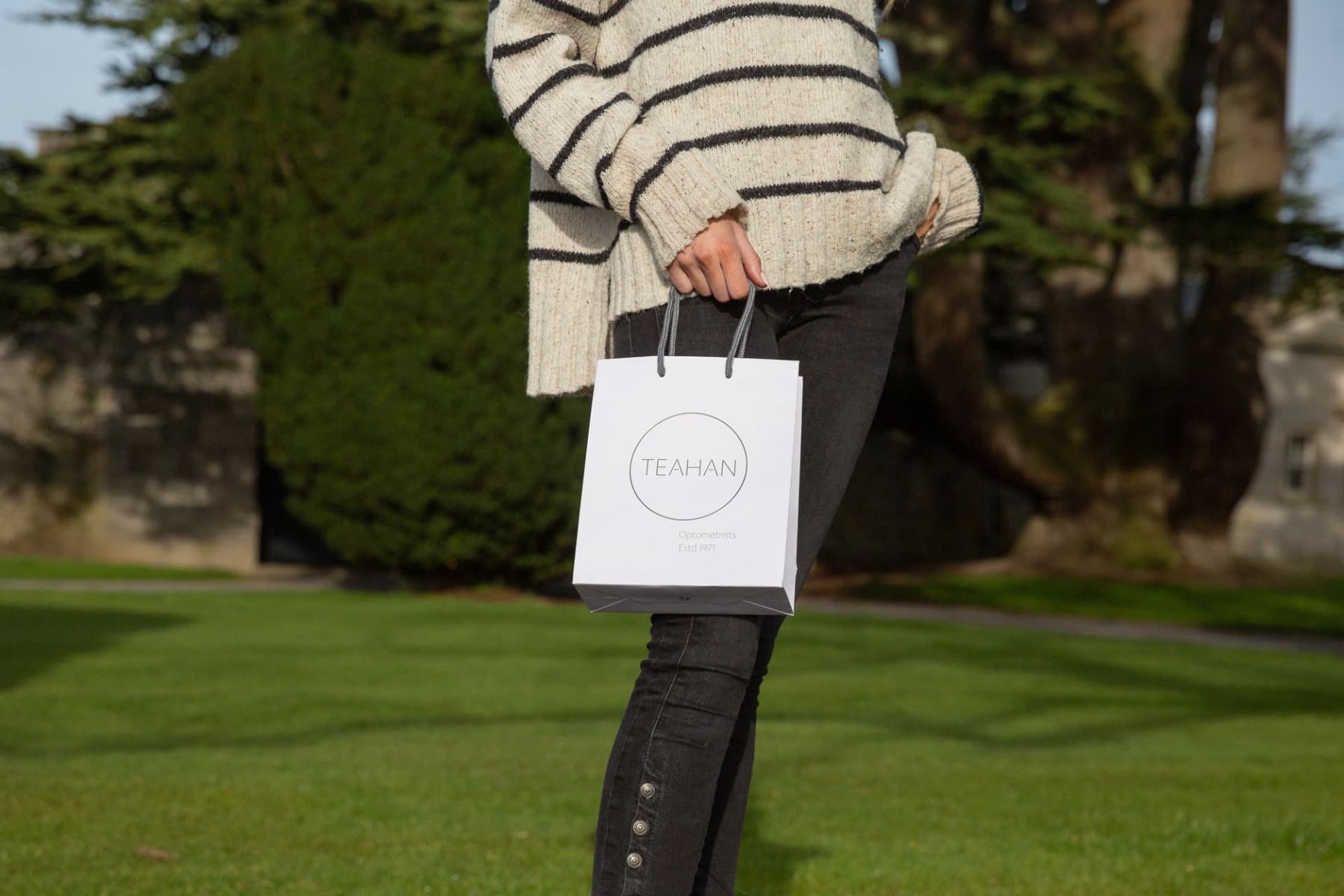Small white matt laminated paper bag with grey logo print and grey rope handles. Portrait format luxury carrier with branding.