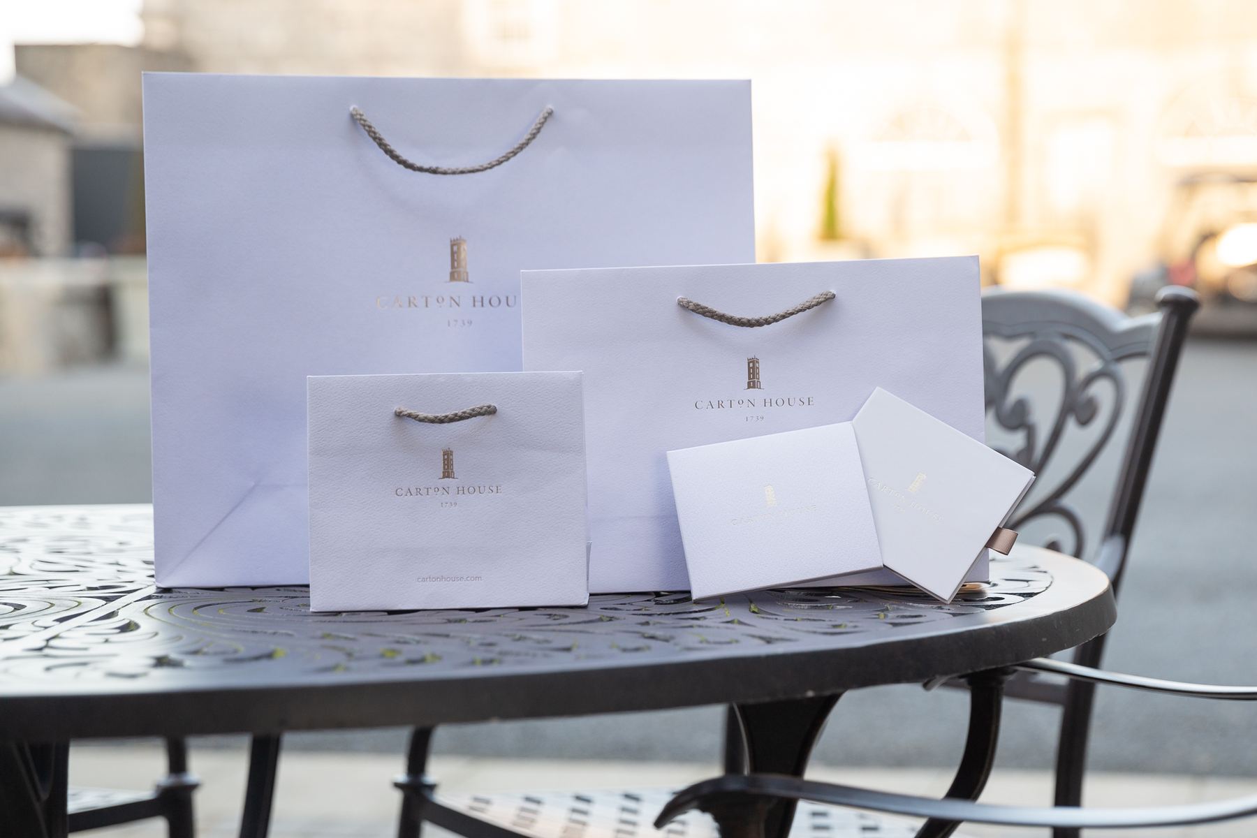 Three white rope handle bags, various sizes. Two white rigid gift boxes with gold foil logos.